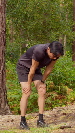 Vertical-Video-Of-Tired-Man-Exercising-Doing-Work-Out-Outdoors-Running-Along-Track-Through-Forest-Stopping-To-Catch-Breath-Shot-In-Real-Time